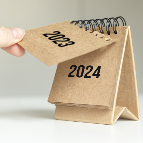 A hand turning over a calendar sheet from 2023 to 2024.